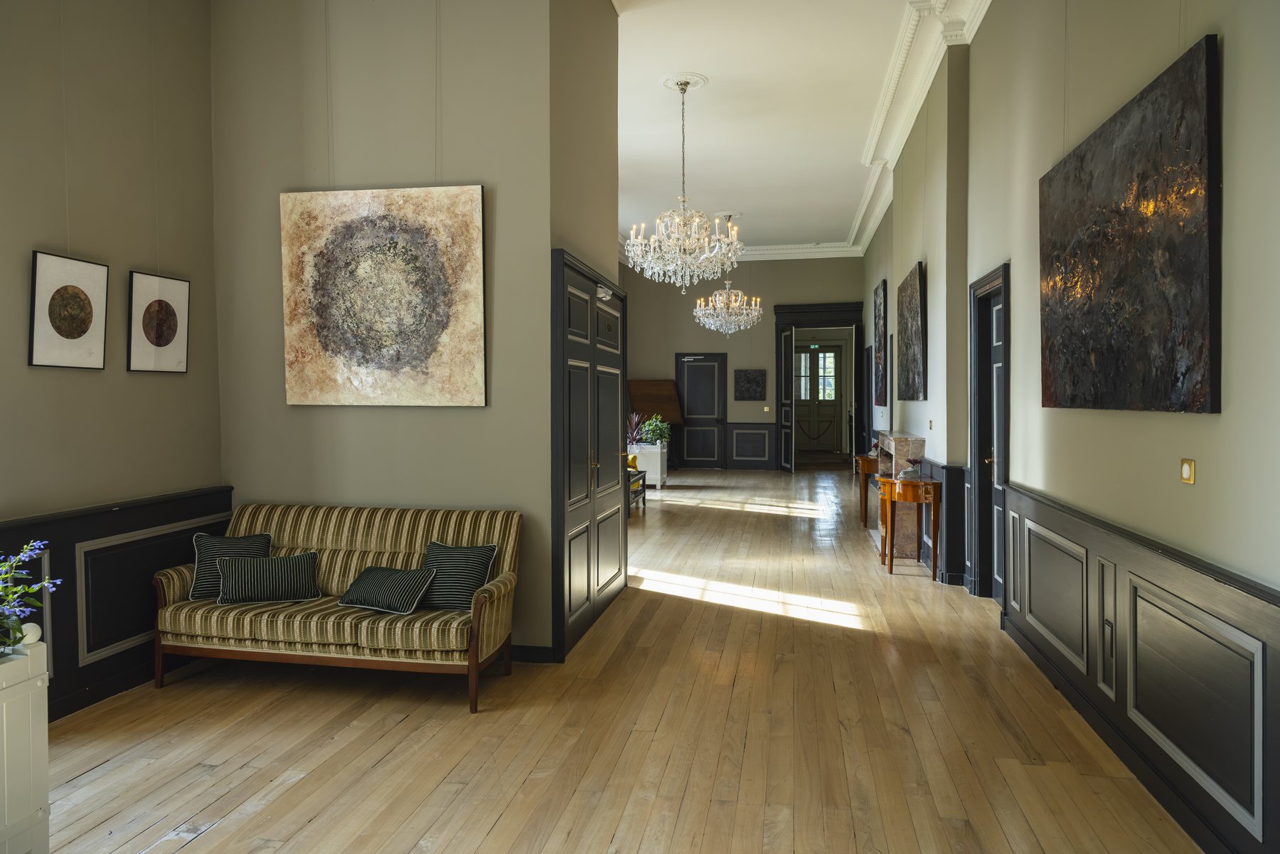 Le hall d’entrée, son long canapé et ses tableaux sous le lustre