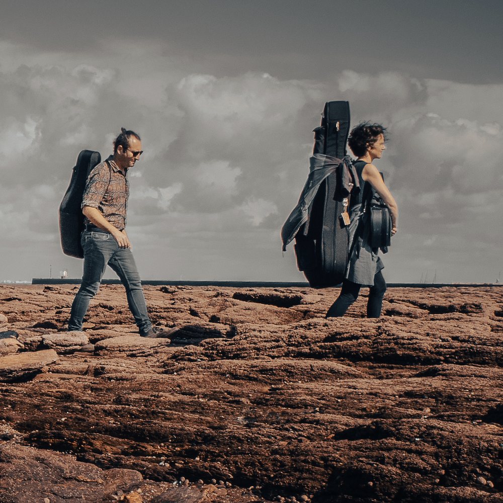 Alban Darche et Myriam Rignol portant leurs instruments le long de la rive